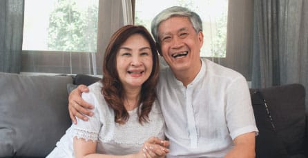 A joyful Asian couple laughing and hugging while sitting on a couch at home
